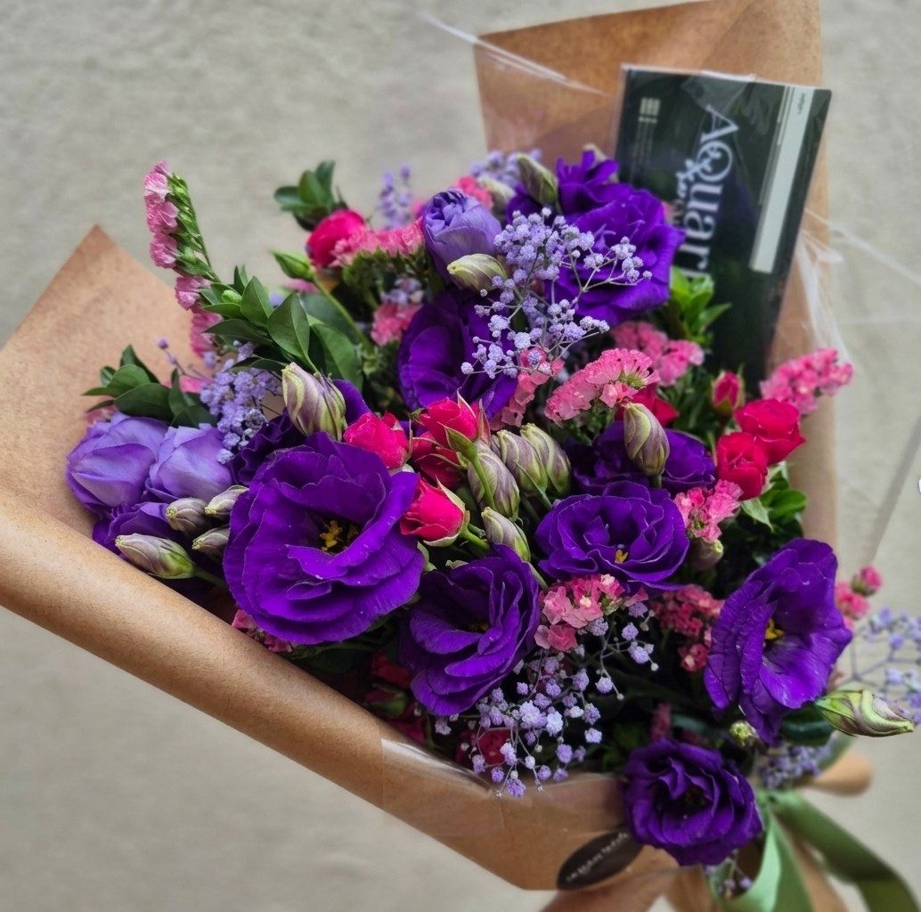 Buquê de lisianthus roxos com mini rosas pink, limônio e mosquitinho lilás, em papel kraft com cartão do Aquarius.